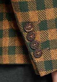 Brązowo-zielona tkanina w kratę z tweedu o teksturowanym wykończeniu, z czterema brązowymi guzikami z grawerowanym detalem na mankiecie.