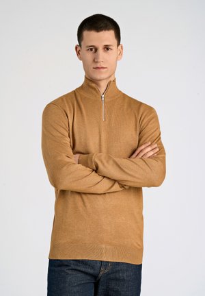 Suéter de cremallera color topo hecho de una tela suave, con un cuello alto y puños acanalados, combinado con jeans oscuros. Diseño sencillo y clásico.