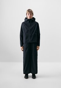 Black waterproof jacket with a hood, zip closure, and loose fit, paired with matching wide-leg trousers. Smooth texture and minimalistic design.