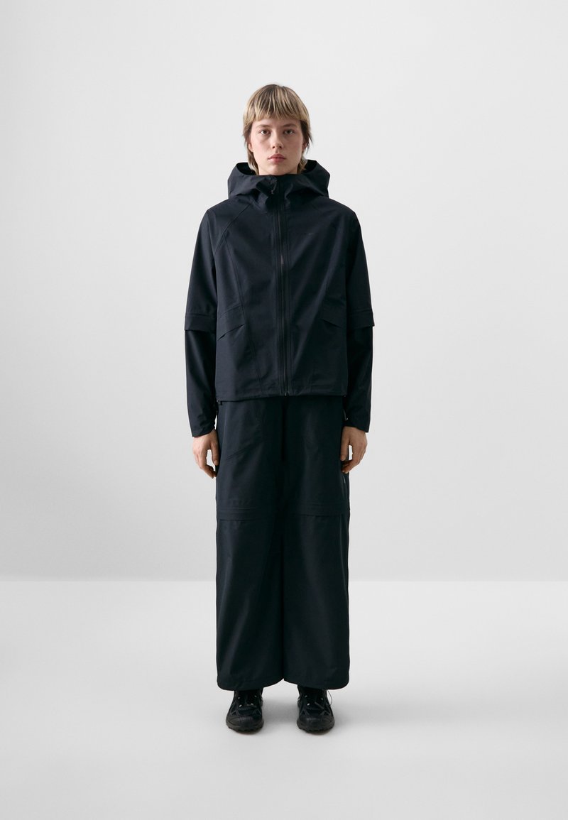 Black waterproof jacket with a hood, zip closure, and loose fit, paired with matching wide-leg trousers. Smooth texture and minimalistic design.