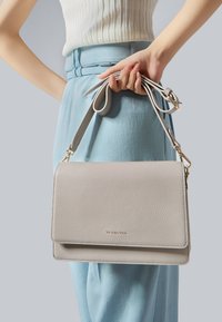 Sac à main en cuir gris clair avec une finition texturée, doté d'un rabat pliable, d'une bandoulière réglable et de quincailleries discrètes en ton doré.