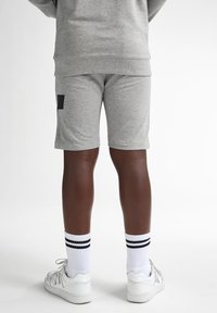 Shorts gris en coton avec un détail de poche noire, associés à des chaussettes blanches à rayures noires et des baskets blanches. Fond neutre blanc.