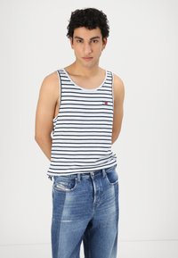 Gestreept tanktop in wit en zwart met een klein rood logo op de zak, gecombineerd met lichtblauwe denim jeans met een klassieke pasvorm en lichte slijtage.