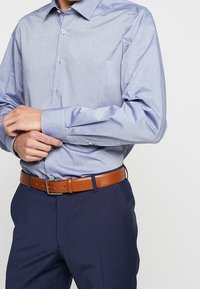 Lichtblauw overhemden met lange mouwen en een gladde textuur, gecombineerd met donkere broek en een leren ceintuur in bruin.