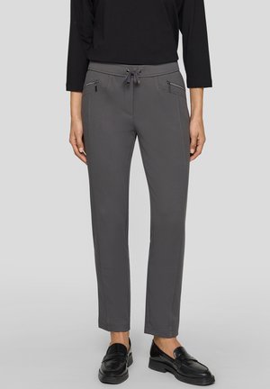 Person wearing gray slim-fit pants with front zipper pockets and black loafers, paired with a black long-sleeve top.