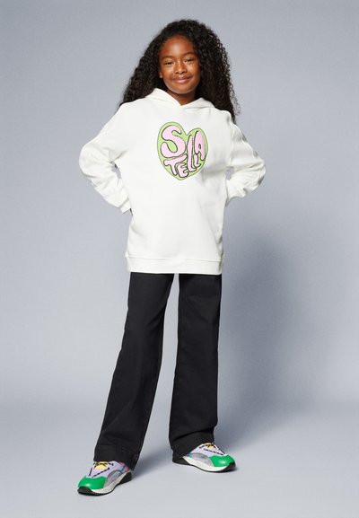 White hoodie with a colorful heart graphic, paired with black pants and multicolored sneakers. The fabric is soft with a relaxed fit.