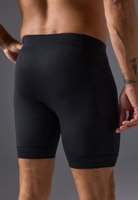 Black athletic shorts made of stretchy fabric, with a fitted design, smooth texture, and subtle stitching detail along the hem and sides.