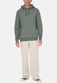 Grøn hoodie med en kengurulomme, ribbede ærmer og kant; parret med beige vidde bukser og sorte sneakers.