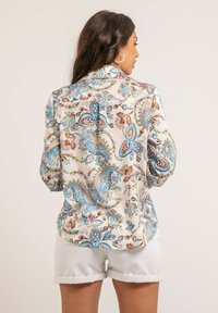 Blouse à manches longues en soie crème avec un motif paisley bleu et marron, dotée d'un col et d'une fermeture à boutons au dos.