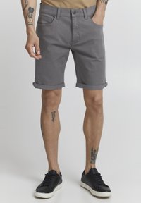 Gray denim shorts with rolled cuffs, front and back pockets, paired with black sneakers. Features visible leg tattoos.
