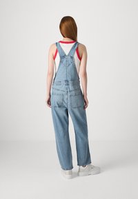 Light blue denim overalls with adjustable straps, wide leg fit, and front and back pockets. Styled over a red and white tank top.