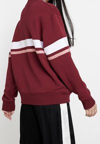 Felpa bordeaux con strisce bianche e rosa, maniche lunghe, vestibilità ampia e polsini a coste. Tessuto morbido, design informale.