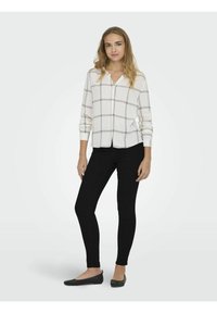 Biely košeľový top s čiernym mriežkovým vzorom, dlhé rukávy, skombinovaný s čiernymi slim-fit nohavicami a plochými čiernymi topánkami. Jednoduchý dizajn, ľahká tkanina.