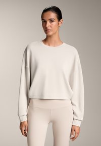 Világos bézs pulóver, laza fazonnal, kerek nyakkal és hosszú ujjakkal, hozzá illő bézs leggingsszel. Puha anyag, minimalista dizájn.