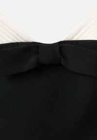 Bodice noire avec une partie supérieure texturée blanche, ornée d'un nœud en tissu noir à l'arrière. Fini lisse et couleurs contrastées.