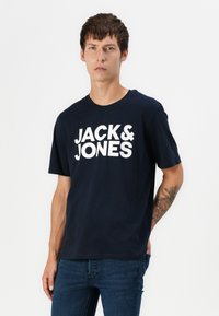Tamsiai mėlyna medvilninė marškinėliai su apvalia iškirpte, priekyje esantis didelis baltas užrašas "JACK & JONES". Trumpomis rankovėmis ir laisvu siluetu.