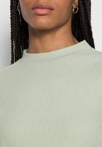 Top ribbed verde chiaro con collo alto e tessuto testurizzato, progettato per una silhouette aderente con dettagli delle cuciture sottili.