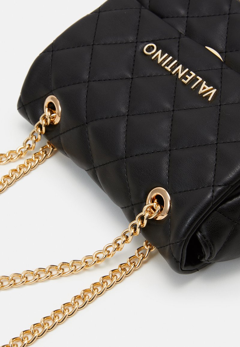 Borsa a tracolla in pelle trapuntata nera con catena e hardware in tonalità oro. Presenta un logo prominente e un design strutturato per un trasporto facile.