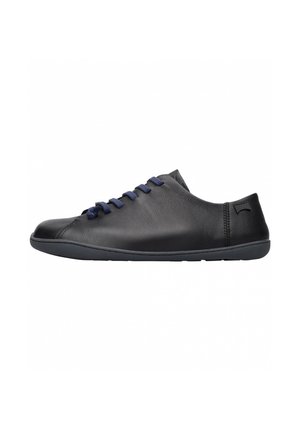 Schwarzer flacher Ledersneaker mit dunkelblauen Schnürsenkeln und flacher Gummisohle, von der Seite vor weißem Hintergrund gesehen.