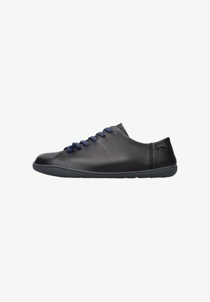 Zapatilla de cuero negra de caña baja con cordones azul marino y suela de goma plana, vista de lado sobre fondo blanco.