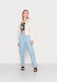 Beige cropped jacket, black and white patterned crop top, light blue drawstring trousers, and black platform sandals.