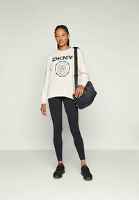 Felpa chiara con logo "DKNY", abbinata a leggings neri e sneakers neri. Contiene una borsa a spalla nera, con motivi minimi.