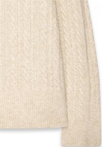 Manche et ourlet de pull tricoté couleur crème avec motifs torsadés et côtes en tissu de laine douce.