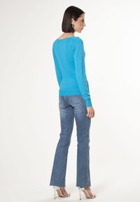 Blauer Pullover aus leichtem Strick mit langen Ärmeln und Rundhalsausschnitt. Kombiniert mit hellblauen Schlagjeans und silbernen Absätzen.