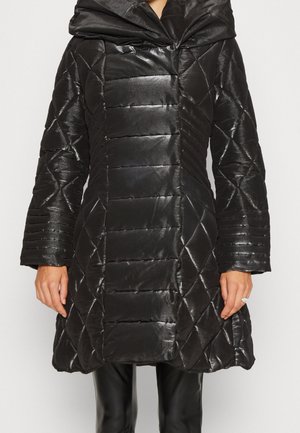 Femme portant un manteau matelassé noir brillant avec des coutures diagonales et horizontales, un large col et un ourlet évasé.