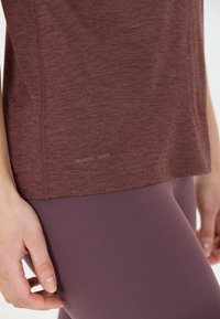 Burgunderröd snabbtorkande topp med en strukturerad finish, med en rundad nederkant och sydda detaljer längst ner. Bärs med mauve leggings.