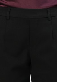 Pantalons noirs ajustés avec une taille plate, une texture lisse et des poches latérales discrètes, conçus avec une taille standard et sans embellissements visibles.