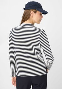 Langärmliges gestreiftes Oberteil mit marineblauen und weißen horizontalen Streifen, rundem Ausschnitt und lockerer Passform. Dazu eine marineblaue Baseballkappe.