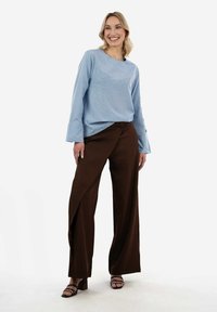 Top azzurro chiaro a costine con maniche lunghe e collo rotondo, abbinato a pantaloni larghi marroni con un design drappeggiato e sandali neri con cinturini.