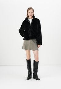 Zwarte nepbont zip-up jasje met hoge kraag, gecombineerd met een geruite rok en kniehooge zwarte leren laarzen.