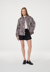Roze panterprint jack met een ontspannen pasvorm, gecombineerd met zwarte shorts met een hartpatroon. Het model draagt zwarte instap schoenen.