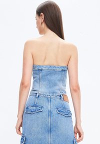 Trikini denim dengan desain pas, warna biru muda, dan kain bertekstur. Tampak belakang menunjukkan hem potongan lurus dan detail tambalan di pinggang.