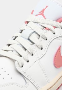 Baskets en cuir blanc avec des accents rose clair, texture à motifs, lacets plats blancs et un logo Air Jordan bien visible sur la languette.