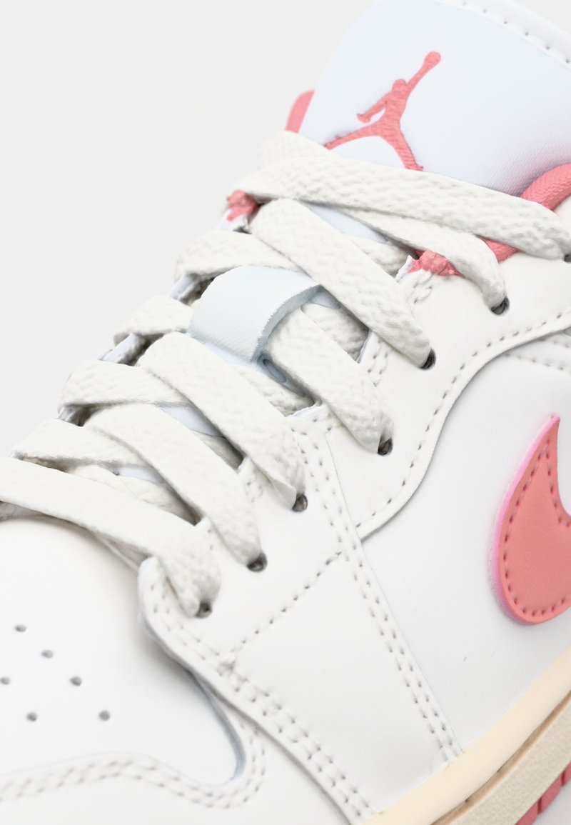 Baskets en cuir blanc avec des accents rose clair, texture à motifs, lacets plats blancs et un logo Air Jordan bien visible sur la languette.