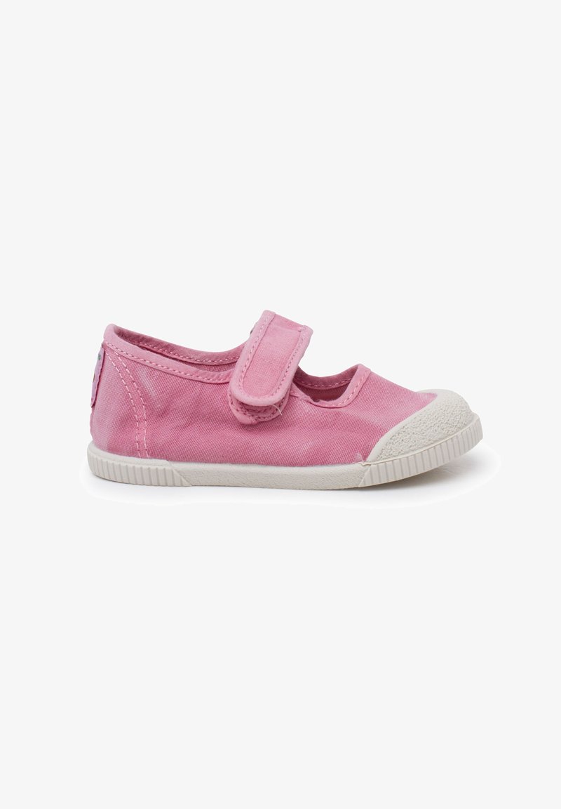Zapato de lona rosa con una correa de velcro, punta redondeada y suela de goma blanca texturizada. Presenta acentos cosidos y un detalle de logo en el costado.