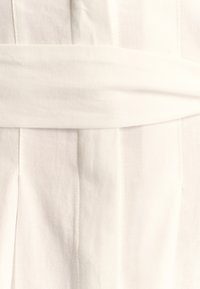 Tessuto bianco con una superficie liscia, caratterizzato da una vita alta e pieghe. Il design enfatizza linee pulite e un'estetica minimalista.