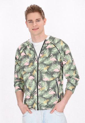 Lichte ritsjack met groene stof, versierd met een patroon van roze flamingo's en tropische bladeren, afgewerkt met zwarte accenten en zakken.