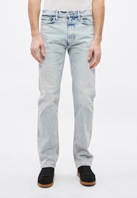 Svijetloplave traperice ravnog kroja, izblijedjelog izgleda, s pet džepova i crnim tenisicama s gumenim potplatom.