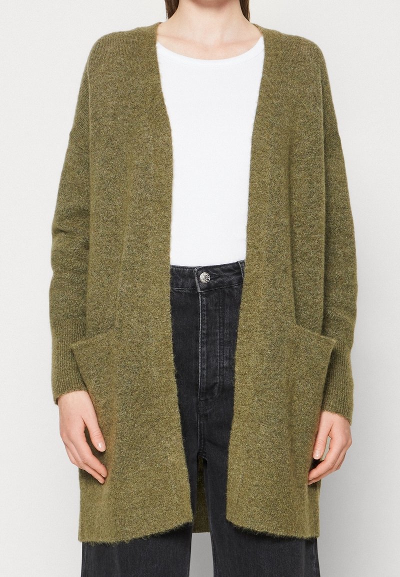 Olivgrön kofta med avslappnad passform, öppen front, långa ärmar och sidofickor, tillverkad av mjukt texturerat tyg.