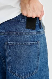 Jeans de mezclilla azul con un acabado texturizado, que cuentan con una etiqueta de cuero negra en el bolsillo trasero y costuras en contraste a lo largo de las costuras.
