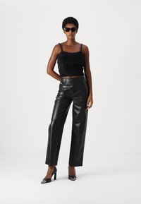 Must have musteljalik faux-fur crop-top õhukeste rihmadega, millele on sobitatud kõrge vöökohaga mustad nahkpüksid. Mudel kannab kassi silmade prille ja kontsakingi.