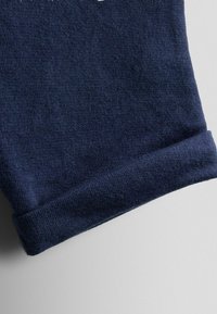 Tumesinise kampsunisärk, valmistatud pehmest kudumiskangast, millel on voltidega serv, sile tekstuur ja väikesed, ühtlased nõelapisted.