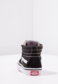 Schwarze Wildleder-Hochtop-Sneaker mit weißen Nähten und Logo, runder Zehenform, gepolstertem Kragen und roter Gummisohle mit Markendetails.