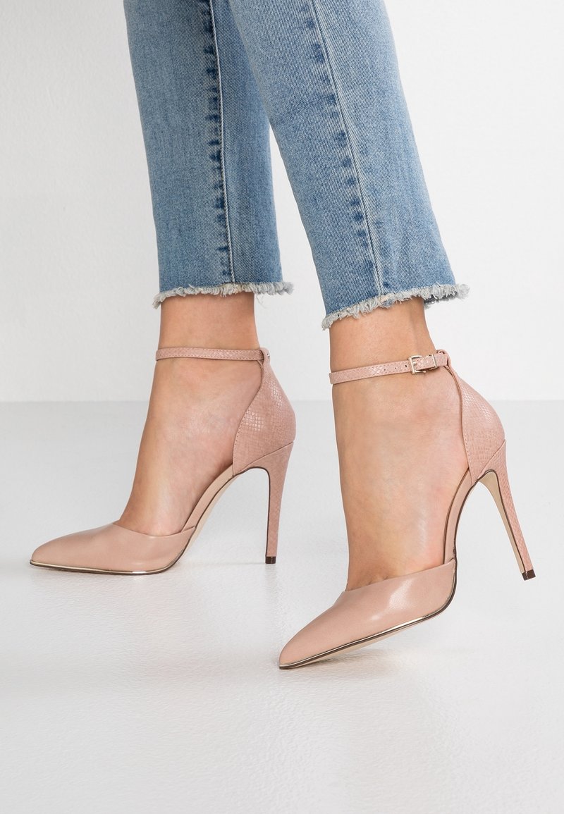Nackte, hochhackige Schuhe mit spitzem Zehenbereich und Slingback-Design, ausgestattet mit einem strukturierten Absatz und einem Schnallenriemen. Glattes Lederfinish.