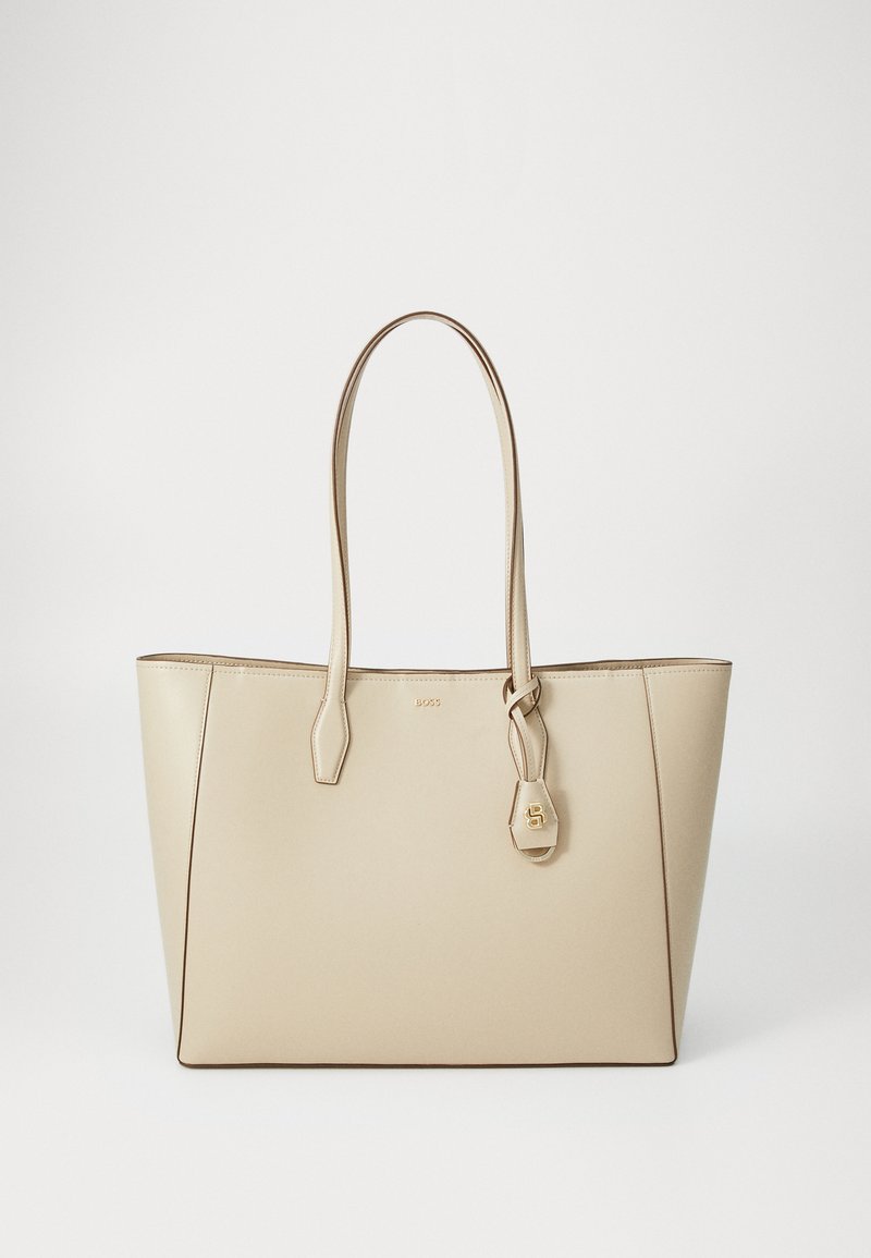 Saco tote de couro bege com duas alças longas, forma retangular, hardware dourado e detalhe da etiqueta com logótipo. Textura suave com costura em contraste.