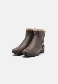 Bottines en simili cuir marron avec doublure en fausse fourrure beige, détail de sangle sur le côté et semelles en caoutchouc plates. Texture lisse, bout arrondi.
